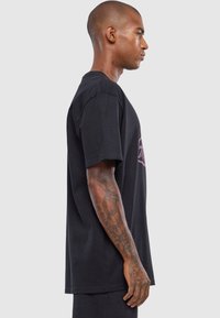 Sort bomulds T-shirt med afslappet pasform, korte ærmer og et sidebillede, der viser tatoveringsdetaljer og enkelt design.