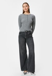 Grijze geribbelde langslavende top met knoopsluiting, gecombineerd met brede donkere jeans en metallic zilveren hakken. Eenvoudig en aansluitend ontwerp.