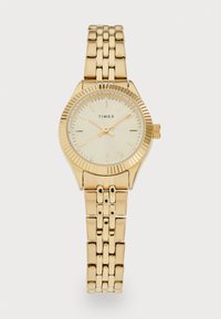 Montre Timex dorée avec un cadran rond et une lunette texturée. Elle dispose d'un bracelet à maillons et d'index horaires minimalistes. Cadran de couleur claire.