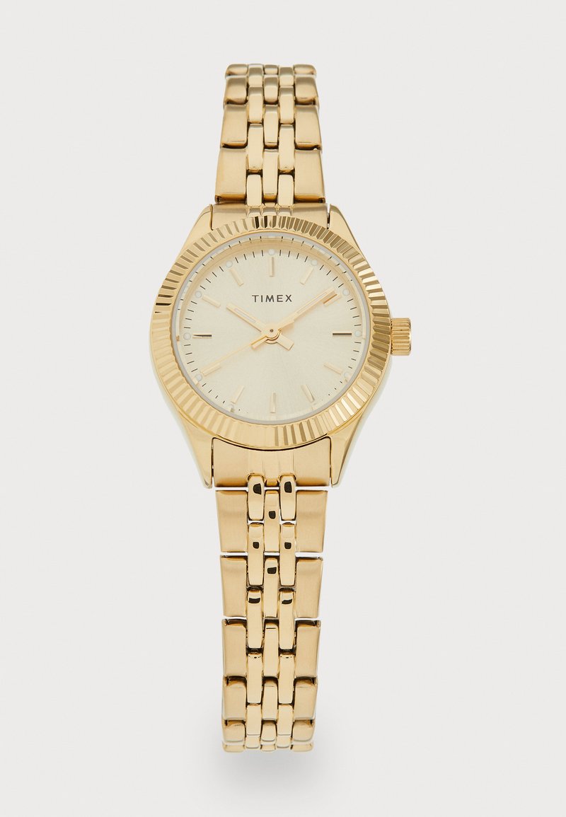 Montre Timex dorée avec un cadran rond et une lunette texturée. Elle dispose d'un bracelet à maillons et d'index horaires minimalistes. Cadran de couleur claire.