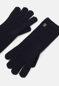 Marineblauwe gebreide handschoenen van zachte stof. Bevat vijf vingers en een klein logo-detail op het polsgebied. Gladde textuur.