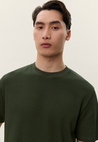 Zelené žebrované tričko s kulatým výstřihem a krátkými rukávy, s texturovanou látkou a volným střihem. Žádné viditelné loga ani vzory.