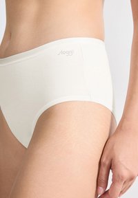 Close-up van een persoon die witte katoen hoge taille onderbroek draagt met het "sloggi" logo op de tailleband, waarbij een deel van de heup en hand zichtbaar is.