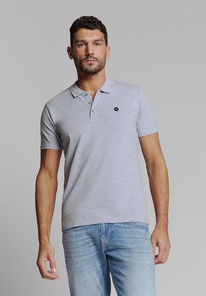 Hellgraues Polohemd mit weicher Textur, Knopfleiste mit zwei Knöpfen und kleinem schwarzem sechseckigem Logo auf der linken Brust. Kombiniert mit blauen Jeans.
