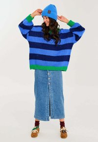 Přehnaně velký pletený svetr s modro-zelenými pruhem, doplněný dlouhou džínsovou sukní s předním zapínáním na knoflíky. Pletená modrá čepice.