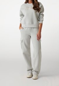 Lichtgrijze sweatshirt en sweatpants set van zachte stof. Het sweatshirt heeft een geborduurd merklogo. De broek heeft cargopockets en een relaxte pasvorm.