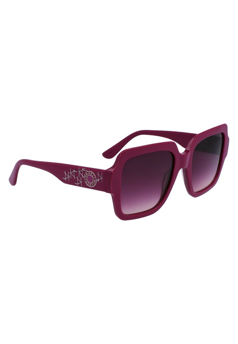 Gafas de sol cuadradas moradas con lentes oscuros degradados y logo decorativo plateado en las patillas, anguladas hacia la derecha sobre un fondo blanco.