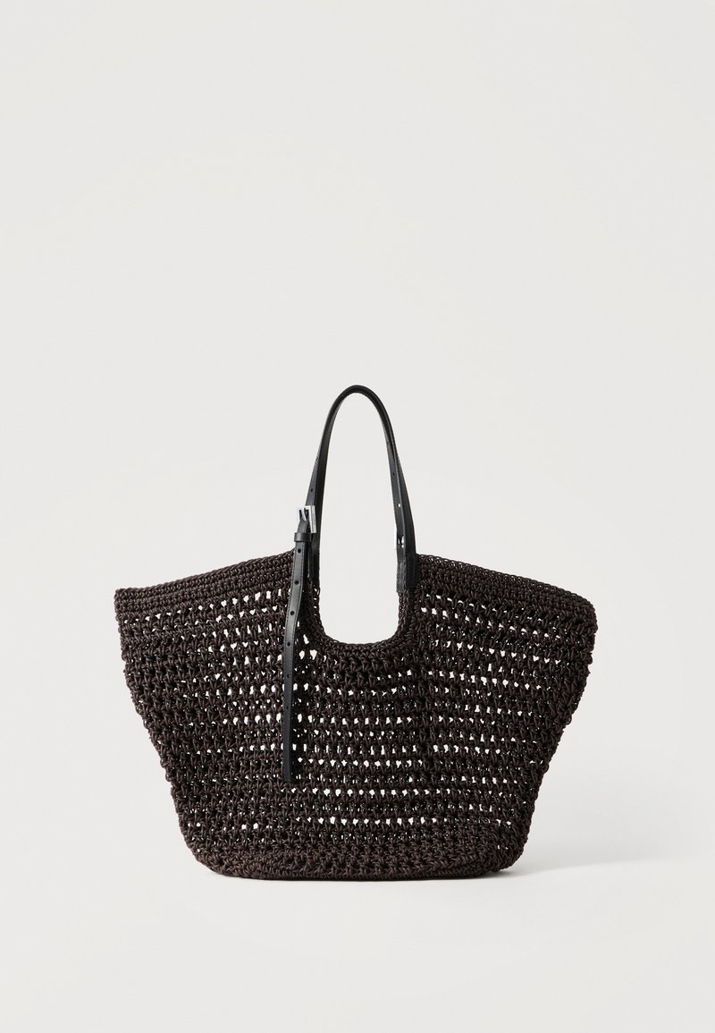 Sac cabas tissé noir avec motif de tissage ouvert et bandoulières en cuir réglables, présenté sur un fond clair uni.