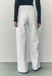 Biele široké rifle s vysokým pásom, so zadnými vreckami a hladkou textúrou látky, v kombinácii s čiernym topom s dlhým rukávom.