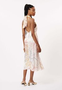 Blumenkleid in Midi-Länge aus leichtem Stoff mit einem tiefen Rückenausschnitt, einer Schleifen-Ausschnittdetail und pastellfarbenen Blumenmustern. Vergoldete Absatzmules runden den Look ab.