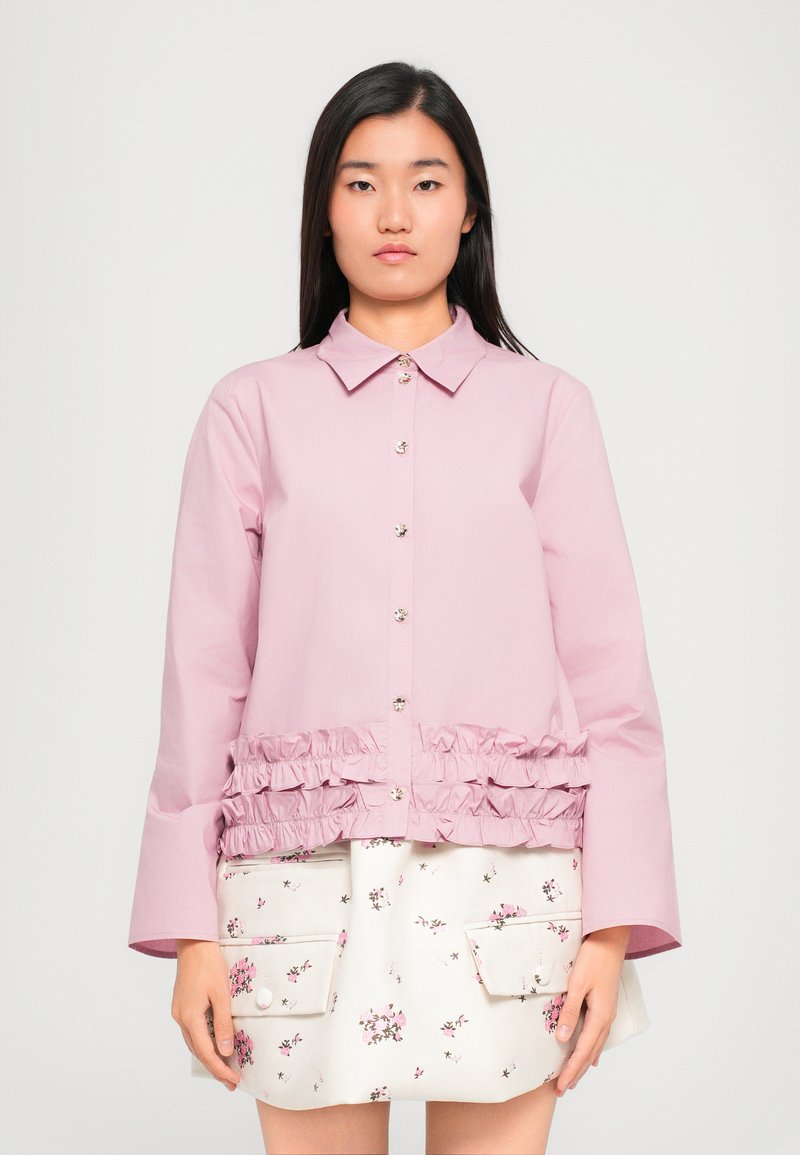 Jasnoróżowa kurtka zapinana na guziki z falbaną u dołu, z wywiniętym kołnierzem i długimi rękawami. Spódnica z kwiecistym wzorem pod spodem.