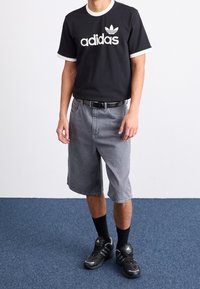 Musta Adidas t-paita valkoisilla yksityiskohdilla ja logolla, harmaat farkkushortsit, musta vyö, mustat sukat ja mustat urheilukengät.