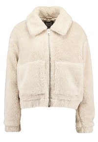 Klippt krämfärgad fleecejacka med krage, framdragkedja och två stora frontfickor; mjukt, strukturerat tyg och ribbad mudd.