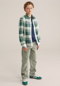 Zeleno-bež karo flanelasta srajca, temno modra majica spodaj, svetlo zelene hlače in teal superge z belimi črtami. Sproščen fit.