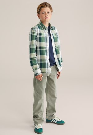 Zielono-biała koszula flanelowa w kratę, granatowy t-shirt pod spodem, jasnooliwkowe spodnie i turkusowe sneakersy z białymi paskami. Swobodny fason.