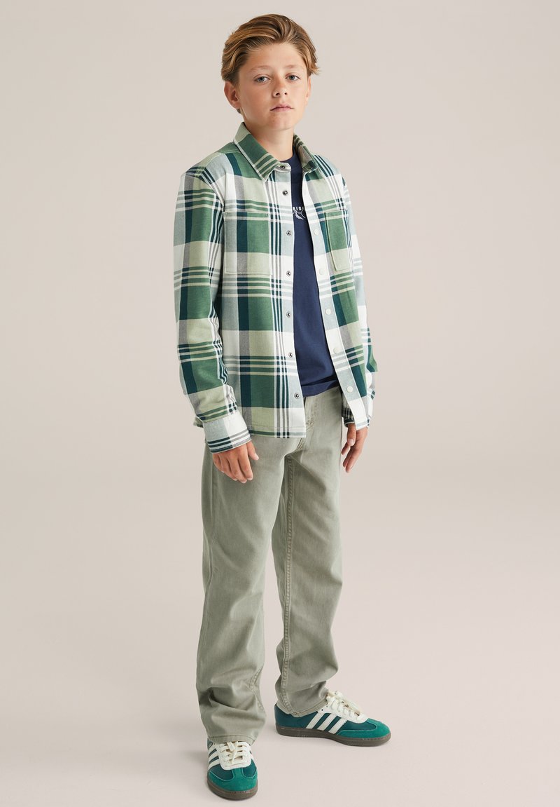 Zeleno-bež karo flanelasta srajca, temno modra majica spodaj, svetlo zelene hlače in teal superge z belimi črtami. Sproščen fit.