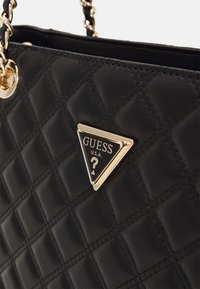 Black quilted handbag made of textured faux leather. Features a prominent gold-tone triangular logo plate with a question mark. Chain handle accents.