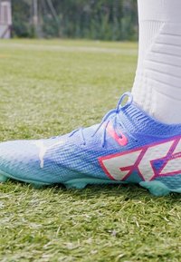 Blå och rosa fotbollssko med en strukturerad mesh-övre, djärv logodesign och formarstövlar för grepp på gräsytor.