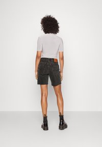 Schwarze Jeans-Shorts mit fransigem Saum, mittlerer Bundhöhe, Gesäßtaschen und braunem Lederpatch am Bund, kombiniert mit schwarzen Stiefeln.