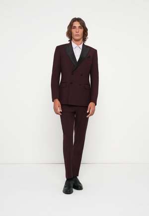 Burgundy dubbelknäppt kostym med svarta satinrevers, matchande byxor och en ljusrosa skjorta. Svarta skor fulländar outfiten.
