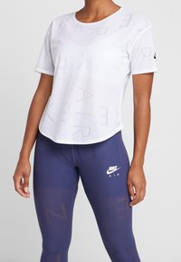 Vit nät-t-shirt med subtil tryck, kombinerad med mörkblå leggings med en texturerad design och en vit Nike-logga på höften.
