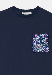 Sweatshirt en coton navy avec une poche frontale ornée de sequins multicolores en motif spiralé. Encolure côtelée pour une texture ajoutée.