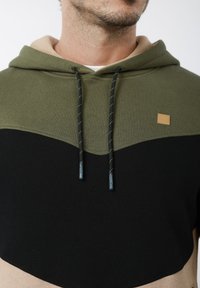 Φούτερ με κουκούλα που διαθέτει σχέδιο με μπλοκ χρωμάτων σε ελιά πράσινο, μπεζ και μαύρο. Υφή υφάσματος με αντίθετα κορδόνια και λογότυπο.