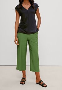 Top blu navy con scollo a V e maniche corte, abbinato a pantaloni verdi a gamba larga. Il modello indossa sandali neri a ciabatta. Tessuto liscio, design casual.