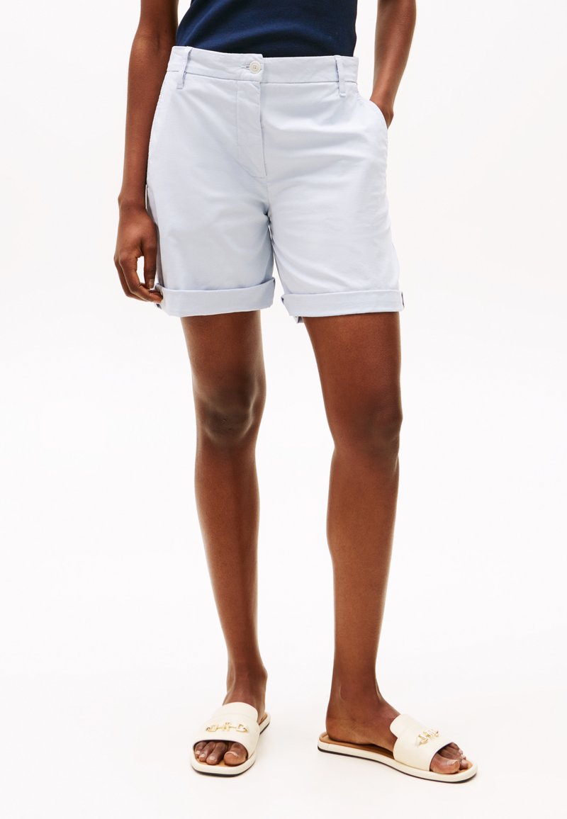 Shorts din bumbac de culoare albastru deschis, cu manșete răsucite, buzunare frontale și închidere cu nasture, asortați cu sandalieri crem cu un accent decorativ.