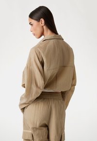 Korte beige jas van een gestructureerde, lichtgewicht stof met een klassieke kraag, gecombineerd met bijpassende cargo-broeken met zijzakken.
