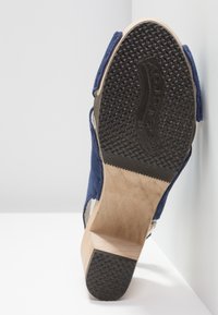 Chaussure à talons hauts en daim bleu avec une semelle en caoutchouc noir texturé et un talon en bois. Dotée d'un dos ouvert et d'une sangle ajustable.