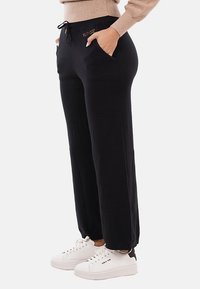 Pantaloni jogger neri a vita alta con finitura testurizzata, dotati di tasche laterali e vita con cordino, abbinati a sneakers bianche.