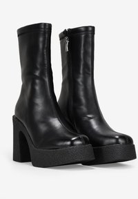 Bottines en cuir noir avec une texture lisse, dotées d'une semelle compensée haute et d'un talon épais ; zip latéral pour la fermeture.