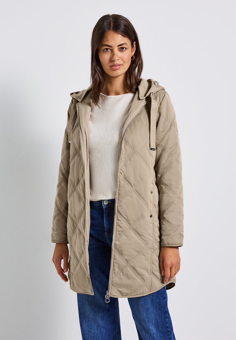 Beige gewatteerde lange jas met een capuchon, voorzien van drukknoopsluitingen, zijzakken en een gestructureerde matte afwerking. Gestyled met blauwe jeans.