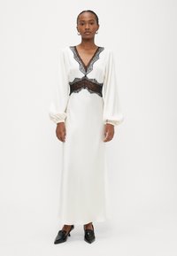 Gara zilo krēmkrāsas kleita ar caurspīdīgām melnām mežģīnēm pie izgriezuma un vidukļa. Kleitai ir gari pūderveida piedurknes un gluda satīna tekstūra. Melni apavi.