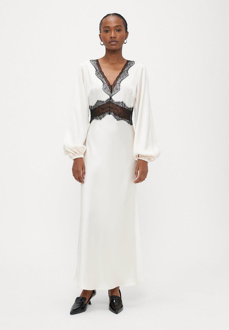 Gara zilo krēmkrāsas kleita ar caurspīdīgām melnām mežģīnēm pie izgriezuma un vidukļa. Kleitai ir gari pūderveida piedurknes un gluda satīna tekstūra. Melni apavi.