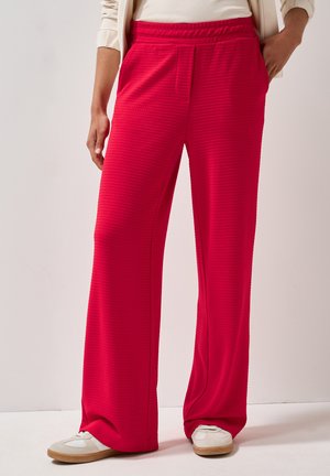 Pantalons larges rouges en tissu texturé, dotés d'une taille élastique, de poches latérales et d'une coupe décontractée, associés à des baskets blanches.