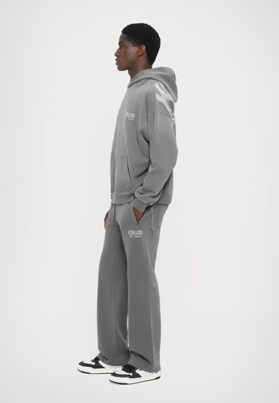 Gray hoodie and matching joggers made of soft cotton. Features a front pocket, logo on the chest, and a relaxed fit with wide legs.