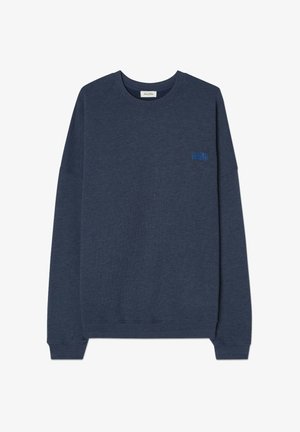 Jūras spēku džemperis, kas izgatavots no mīksta auduma, ar apaļu kakla izgriezumu, garām piedurknēm un nelielu zilu emblēmu kreisajā krūtī.