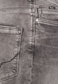 Lähetä lähikuva haalistuneista harmaista farkuista, joiden takataskuissa on eriväriset tikkaukset ja pienet metalliset merkkilaput vasemmassa ja oikeassa taskussa.