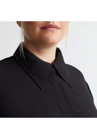 Schwarzes Hemd mit klassischem Kragen, das eine glatte Textur und klare Linien aufweist, mit einer verdeckten Knopfleiste und minimalistischen Designdetails.