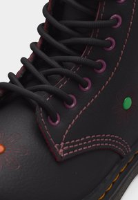 Μαύρο δερμάτινο μπότες με μοβ τρύπες κορδονιών και ραφές, μαύρα κορδόνια και κεντημένα σχέδια λουλουδιών με πολύχρωμα κέντρα στο πλάι.