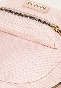 Borsa intrecciata rosa chiaro con una texture liscia, una zip dorata e un flap rettangolare. Include un'etichetta di marchio sopra la zip.