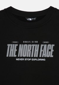 Čierna mikina vyrobená z bavlnenej zmesi s rebrovaným golierom. Na strede je logo v bielej farbe s nápisom "THE NORTH FACE" a "NEVER STOP EXPLORING."