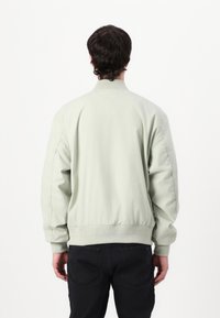 Mintgroene bomberjack met een geribbelde tailleband en manchetten, voorzien van een gladde textuur en een eenvoudig ontwerp. Draagt met donkere jeans.