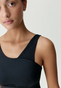 Čierny športový top s širokými ramienkami, hladkou textúrou a priliehavým strihom, ktorý obsahuje jemný šev pri línii krku a na pleciach.