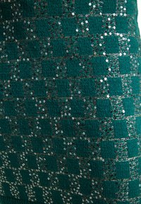 Kangas teal dengan pola bertekstur, dihiasi dengan payet dan benang metalik membentuk desain kisi. Setiap kotak menampilkan rincian yang berkilau.