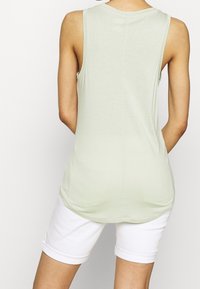 Světl zelený top bez rukávů vyrobený z měkké tkaniny, s kulatým výstřihem a zakřiveným lemem, spojení s bílými zkrácenými šortkami.