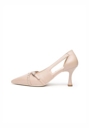 Beiger High Heel Schuh mit spitz zulaufender Spitze, seitlichen Ausschnitten, einem schlanken Riemen mit Schnalle und silbernen Nieten über dem Vorderteil.