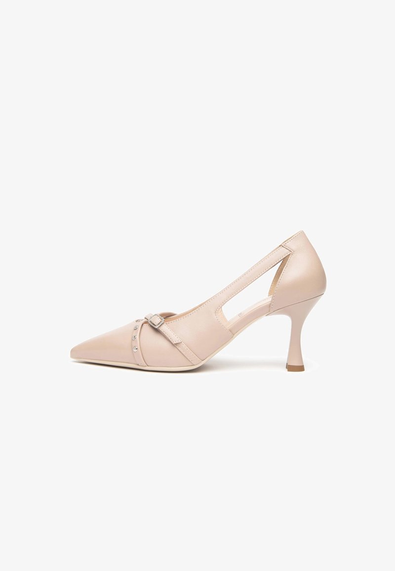 Chaussure à talon haut beige à bout pointu avec découpes latérales, une fine lanière à boucle et des clous argentés sur le devant.